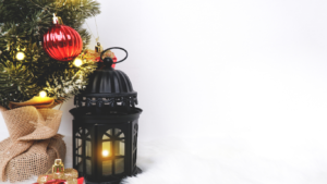A Christmas tree with red ornaments, a glowing black lantern, and wrapped gifts on a snowy backdrop.
