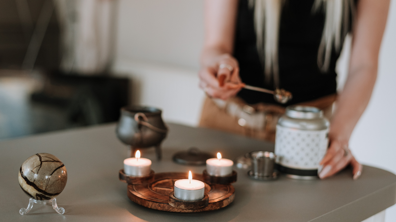 A person adds an ingredient to a pot while candles burn on a wooden tray