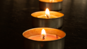 Row of lit tea light candles casting a warm glow against a dark background.