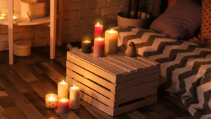 Cozy indoor scene with a wooden crate table, lit candles, and a patterned bed.